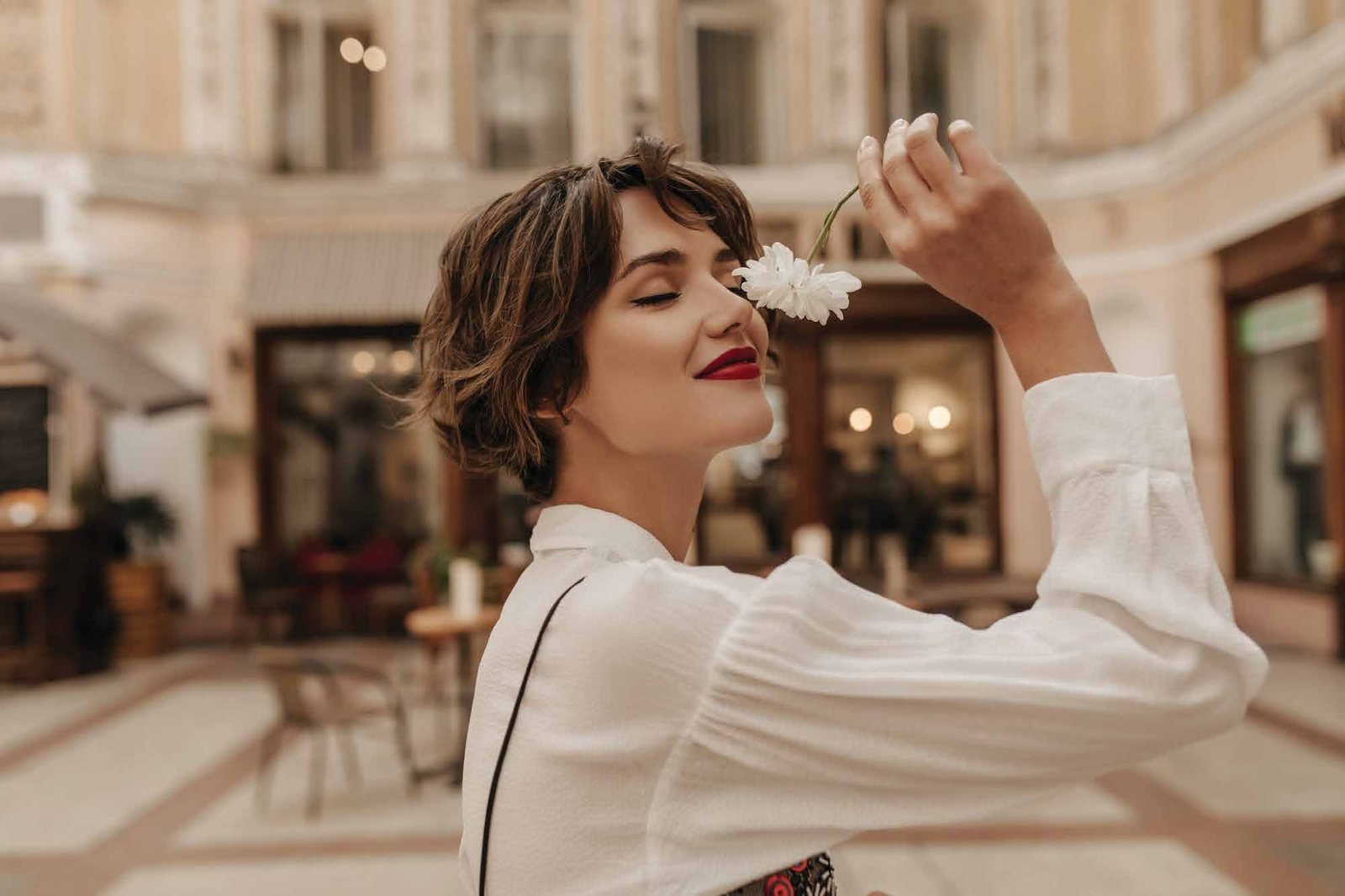 Woman in a white blouse smelling a white flower in an elegant arcade